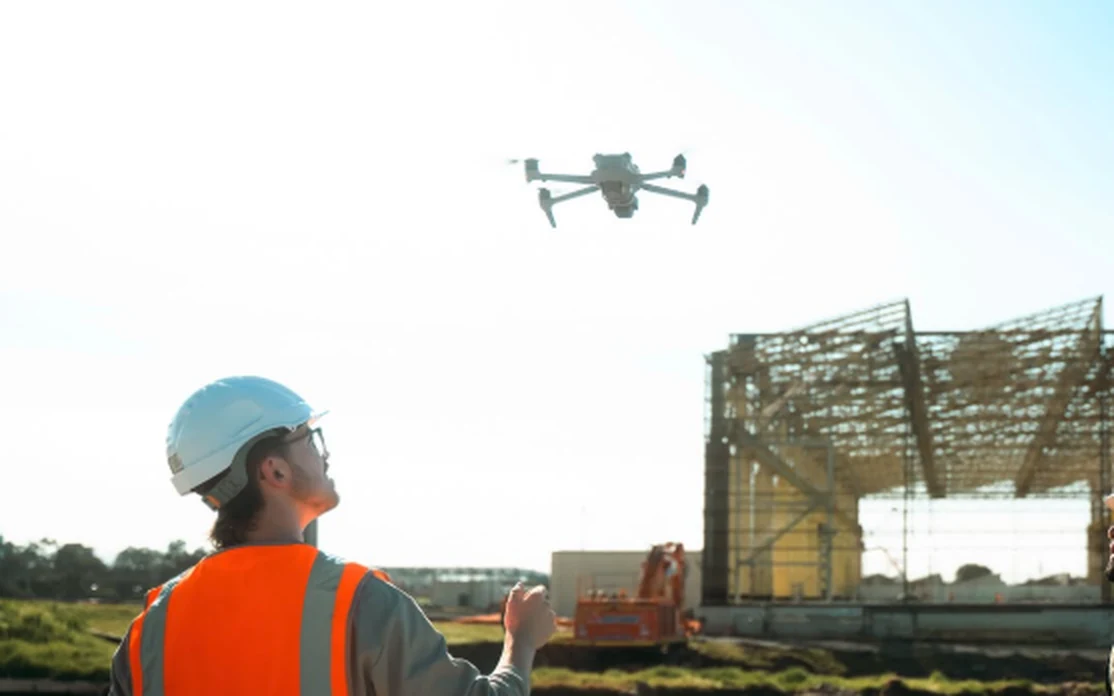 Site worker in a hard hat and hi-vis flying a drone over a Melbourne construction site