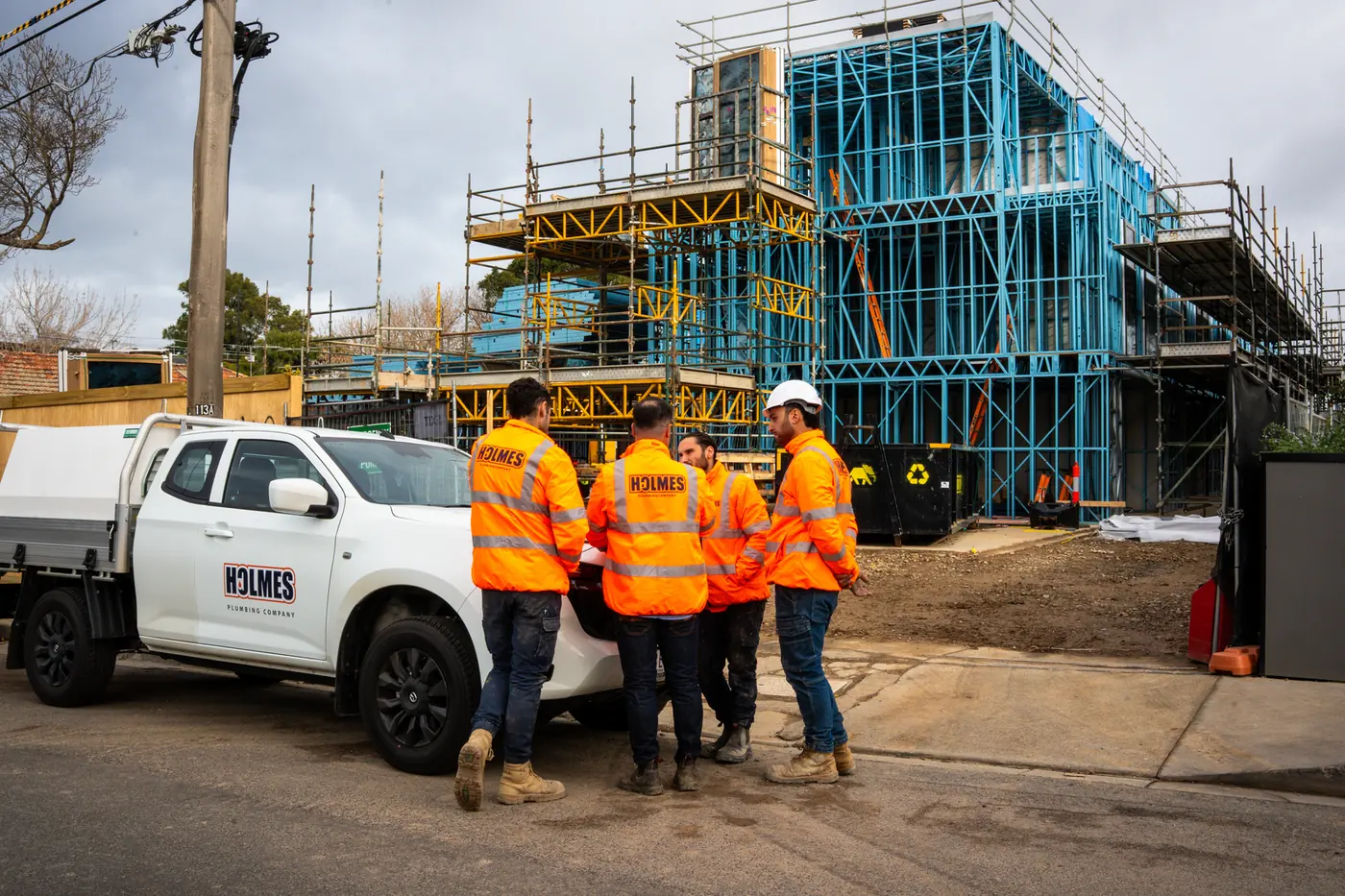 Holmes Plumbing team beside their branded ute in front of the townhouse frames